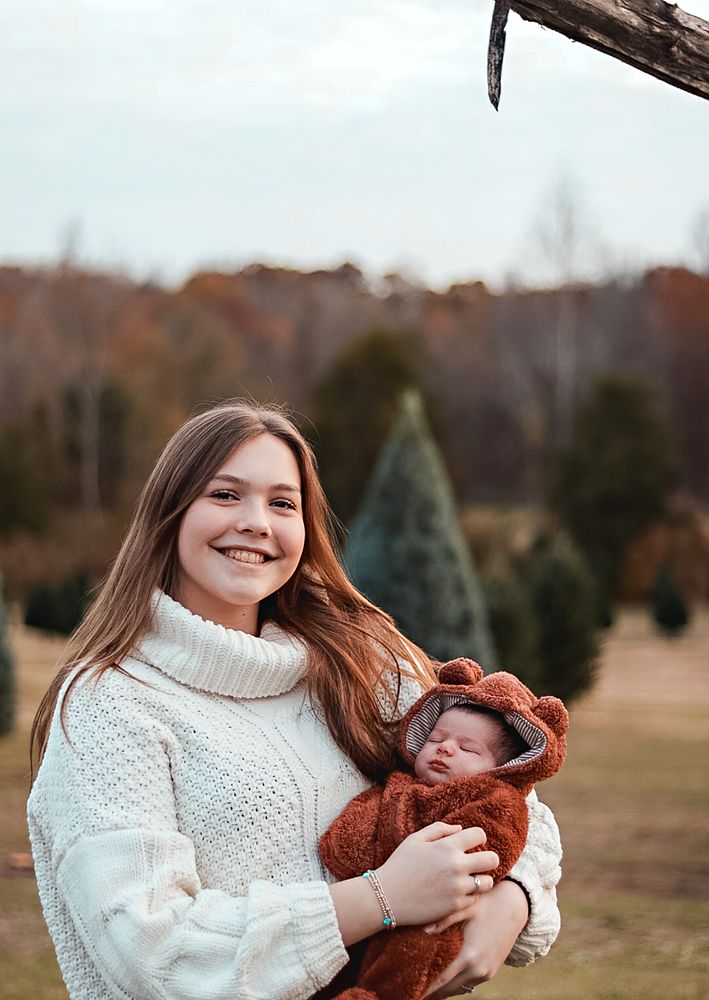 Mom holding her baby in a bear suit at a Christmas tree farm